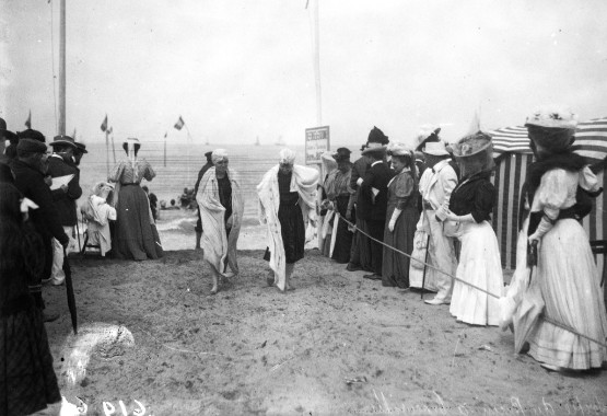 photographie d'une sortie de bain à Trouville : deux femmes en maillots en 1904 sortant de la mer, observées par une foule de curieux